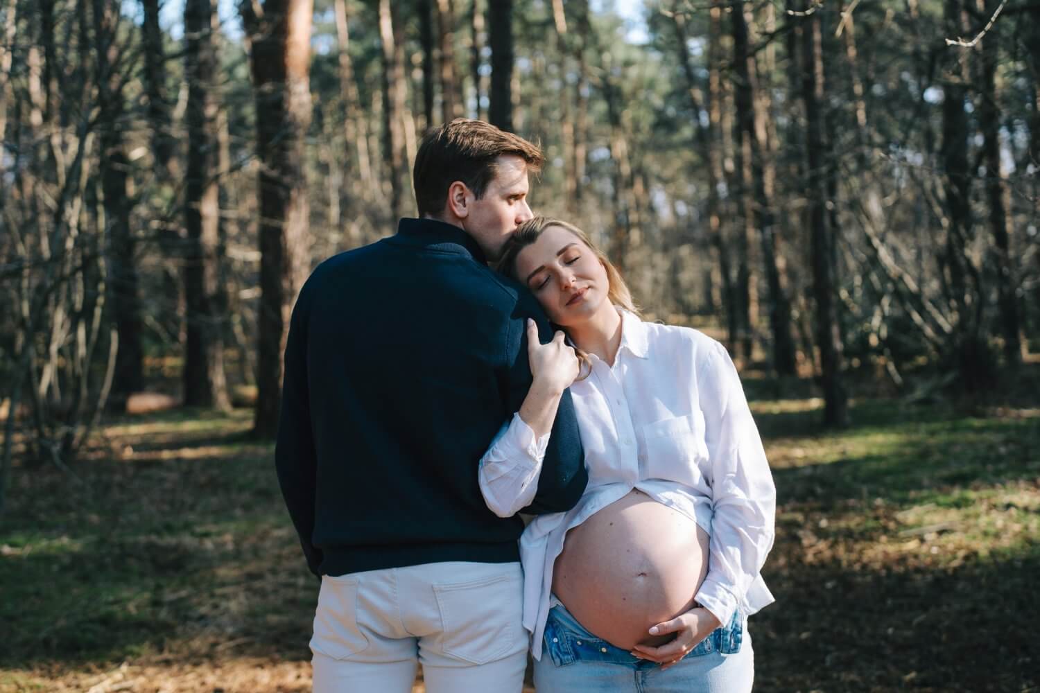 Zwangerschapsfotograaf Keerbergen — koppel in het bos, man kust vrouw terwijl zij haar buik vasthoudt