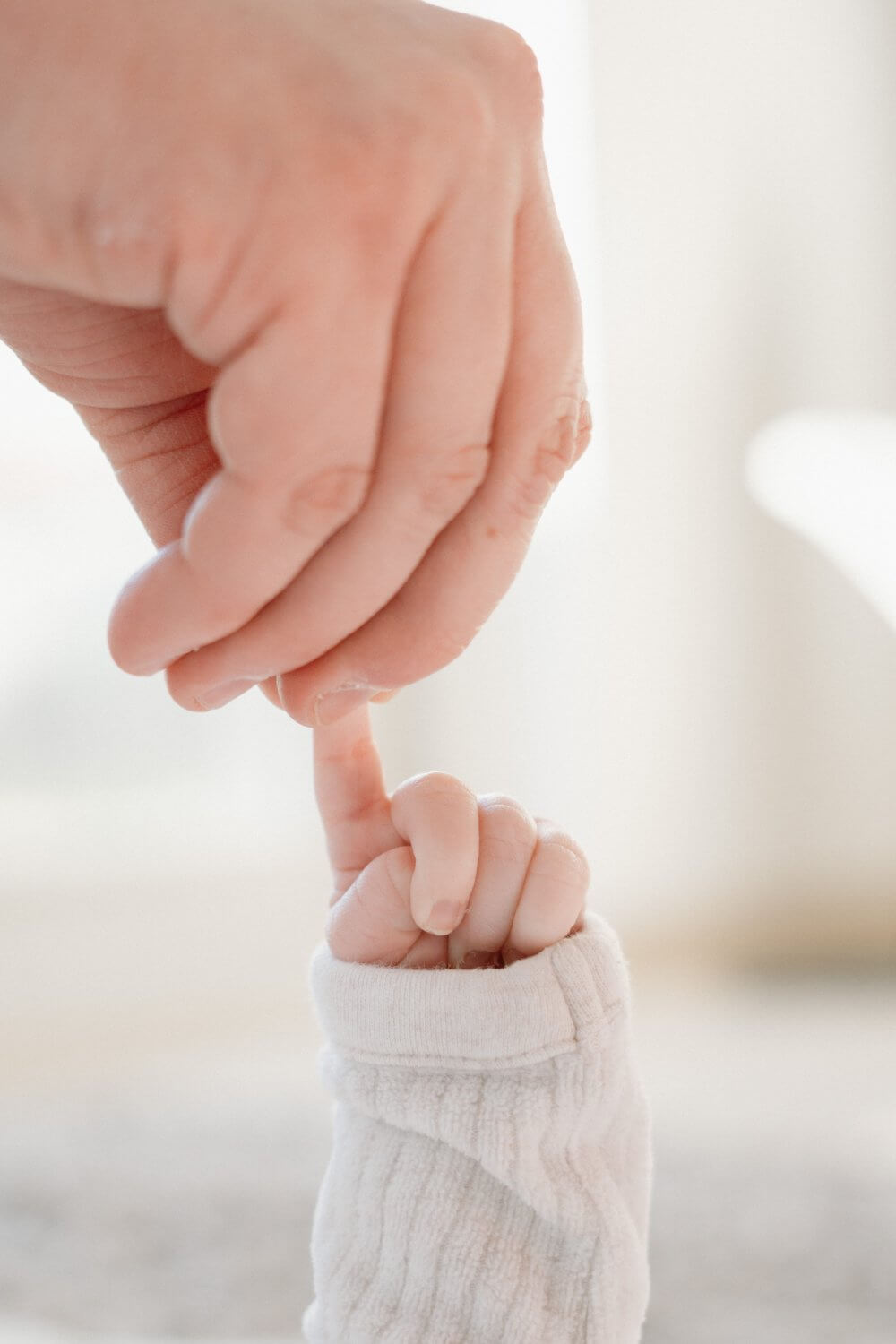 Close-up van een pasgeboren handje dat de vinger van mama vasthoudt — newbornfotografie door Nanou Verhoeven