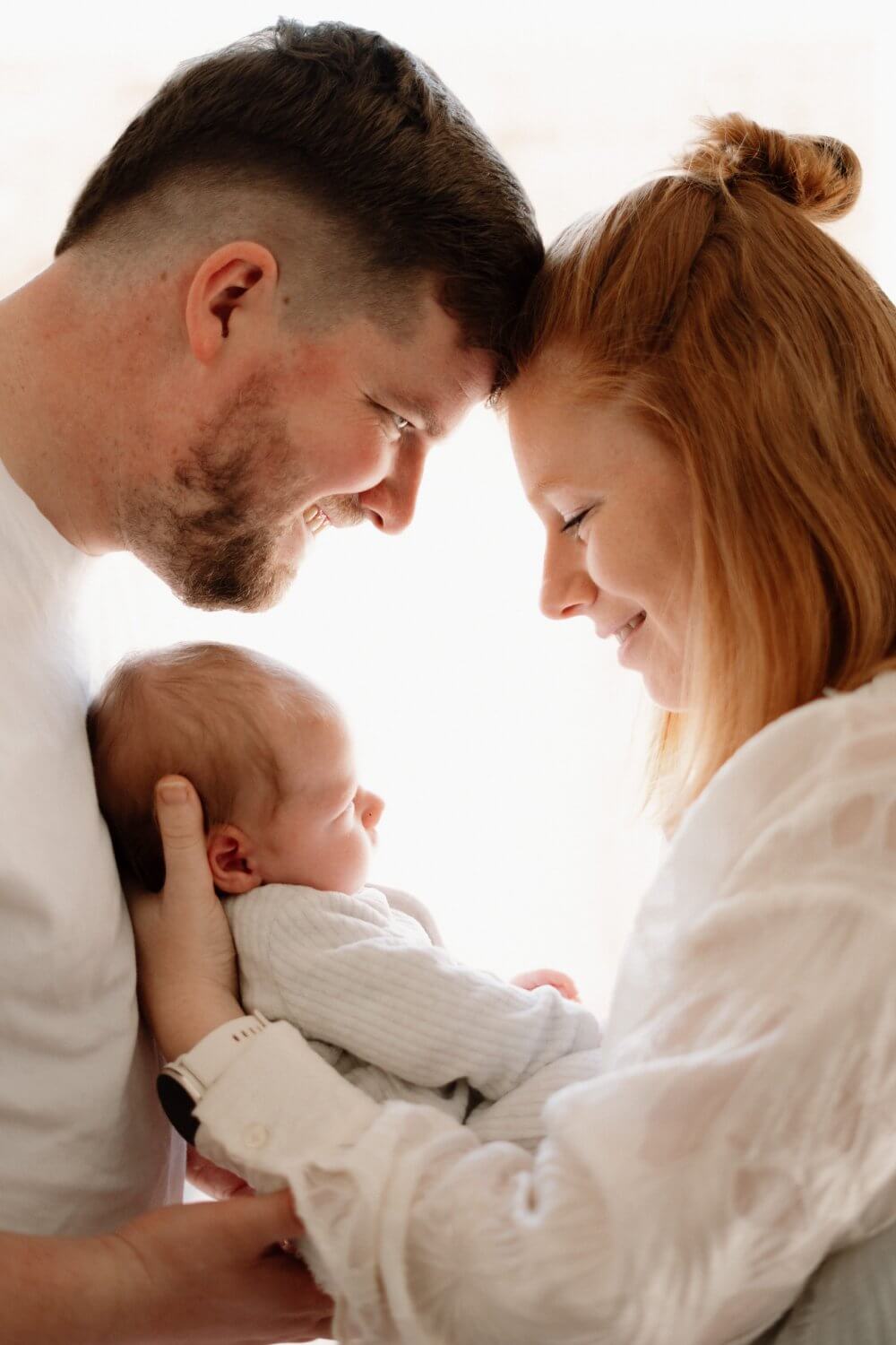 Koppel kijkt glimlachend naar hun slapende newborn — newbornfotografie door Nanou Verhoeven