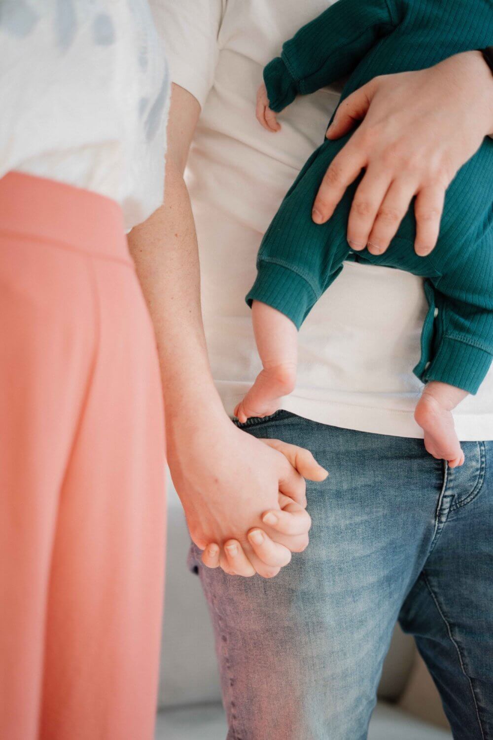 Ouders houden elkaars hand vast terwijl papa de newborn draagt — familiefotografie door Nanou Verhoeven